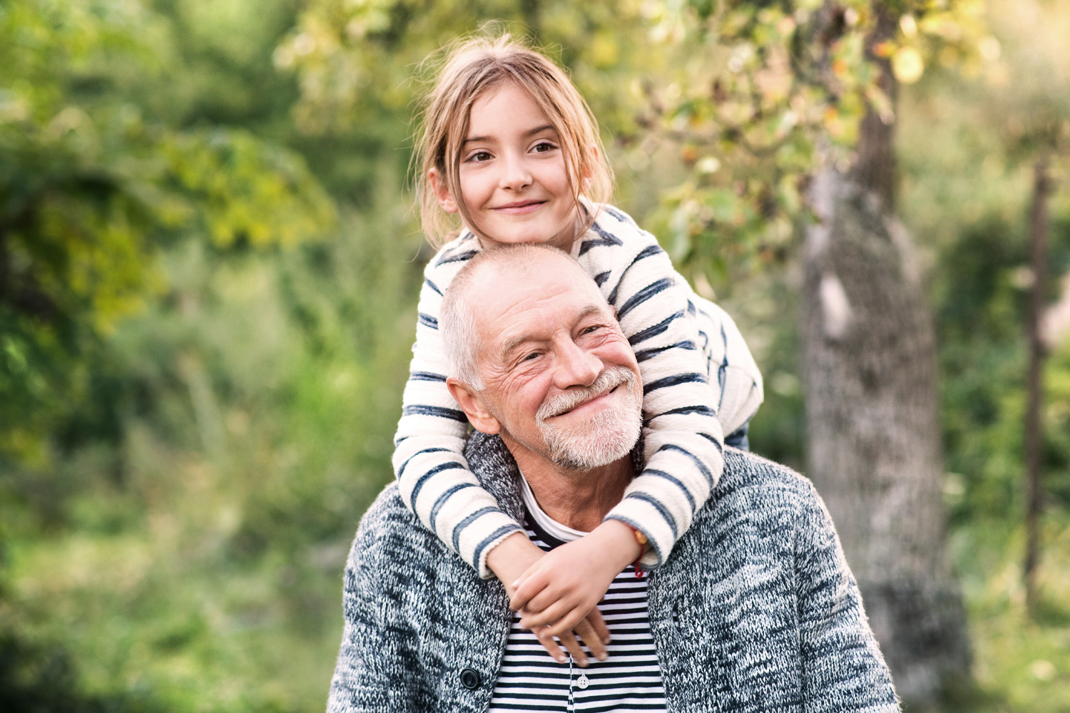 a grandfather giving his granddaughter a piggy back ride and standing in front of a tree